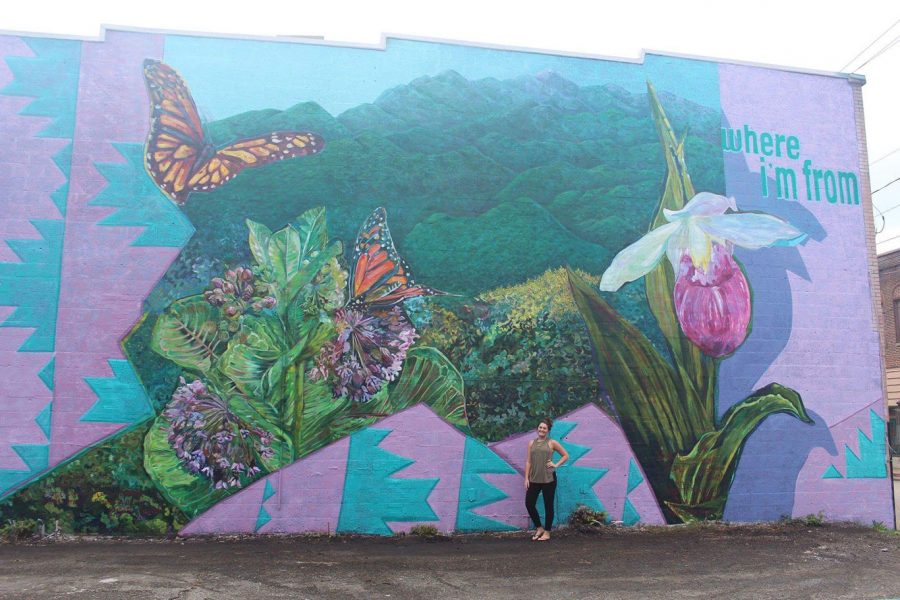 Former Harlan County High School student Emily Eldridge stood in front of the mural recently completed in Cumberland on the side of Buff’s Bows and Gifts. Volunteers spent several days and used quite a bit of paint to complete the project.