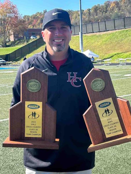 Harlan County cross country coach Ryan Vitatoe is pictured with the girls and boys Region 7 championship trophies. HCHS swept the races on Saturday at Morgan County High School.